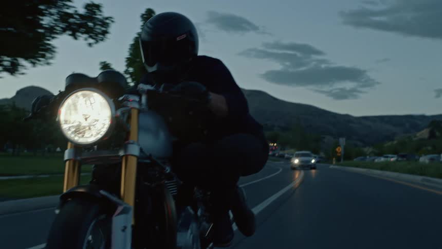 A biker fully kitted doing a bike stunt in the middle of the road with cars coming behind him