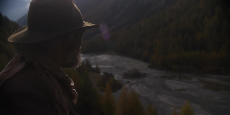 A man stands on a hill and looks down at a river bed as he contemplates