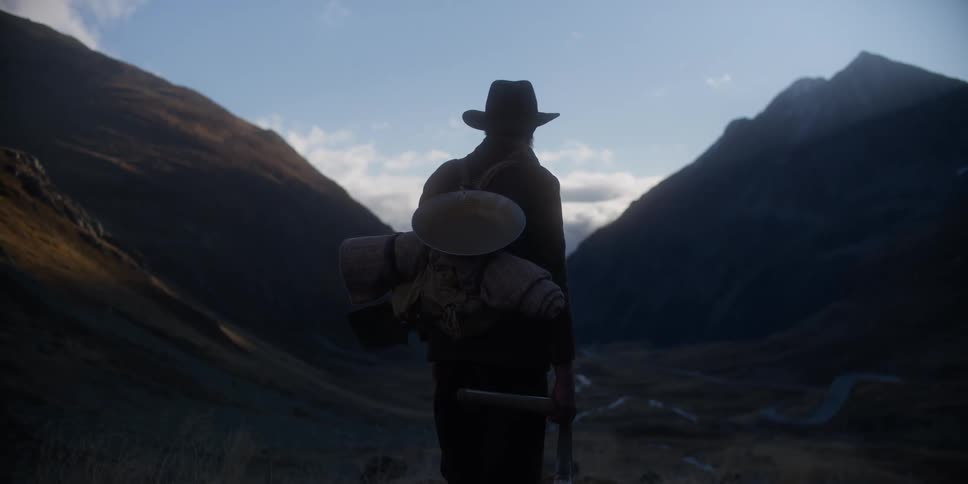 Bearded man wearing a hat and carrying mining tools watching the sky between the mountains in front of him