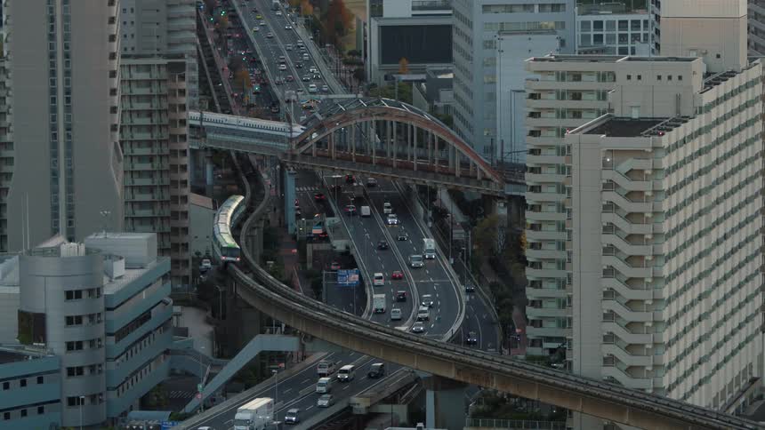 Traffic travels along an overpass through a metropolis while trains pass by overhead on elevated railways