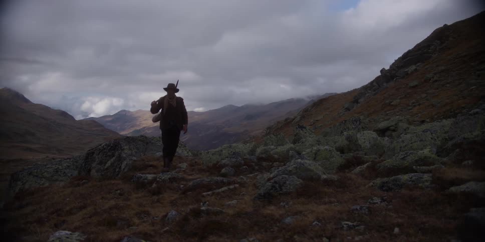 Prospector stops between two hills and stands with pickax on the ground