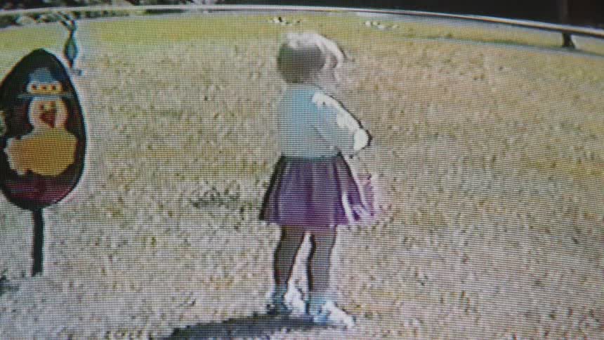 A little girl with a pink easter basket in her hand walking in grass then stopping and spinning around