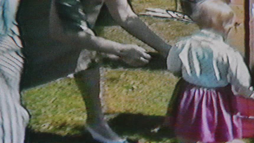A woman helps a young child collect items in a pail as other adults and kids walk past them