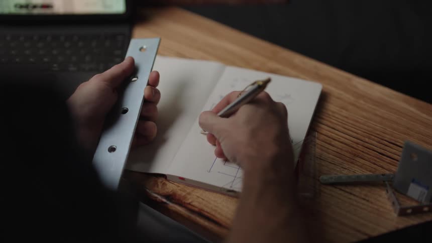 A man holding a ruler and drawing a construction plan in a book with a pen