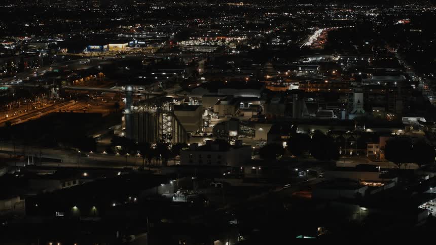 Drone view of a city at night with buildings lit up and traffic traveling on the road