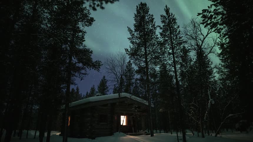 A time lapse view of the northern lights over a snowcovered winter cottage in a forest