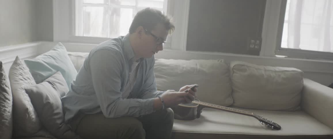 A man sits on a couch and plays a guitar