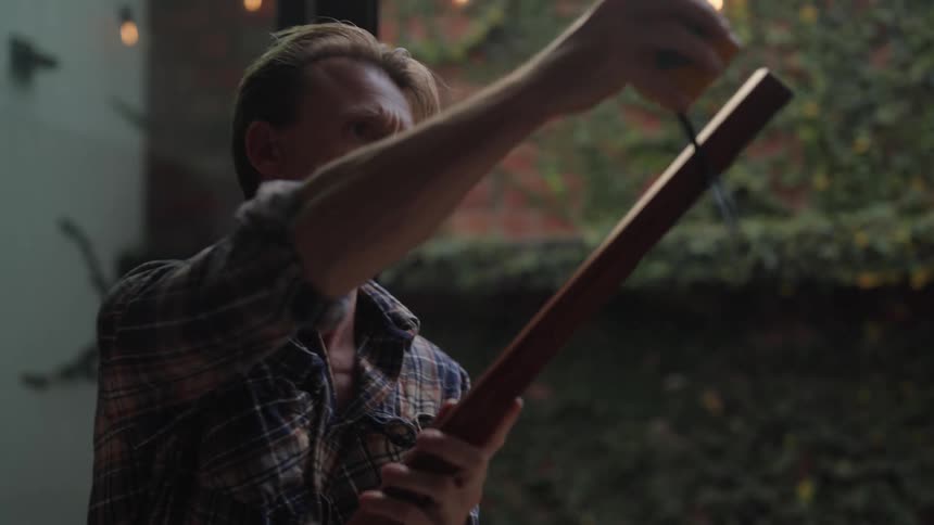 A man is outside measuring a wooden plank with a tape measure
