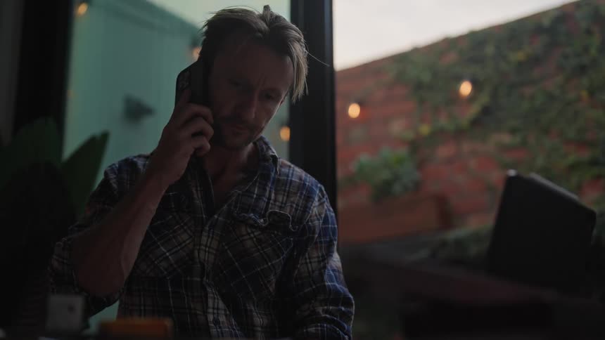 A man is talking on his phone and standing near a window