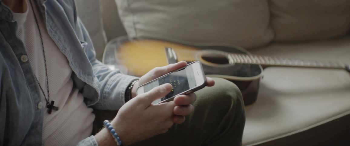 A person sits using their phone by a guitar