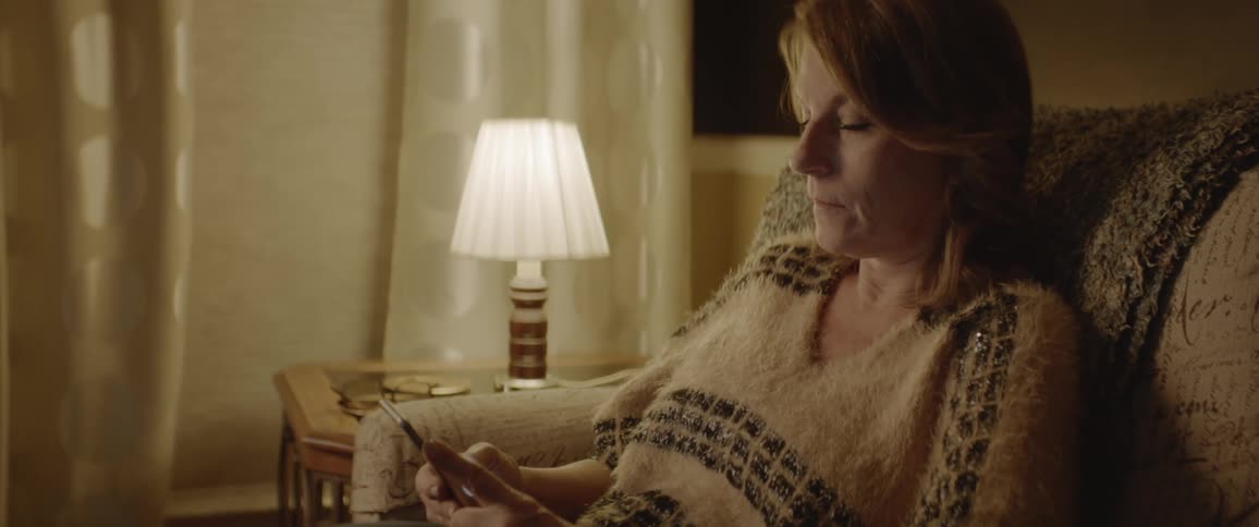 A woman sits on her couch looking at her phone