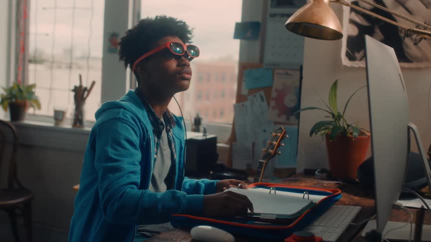 Teenage boy sitting at a computer desk wearing a pair of vr glasses waving his hand in the air