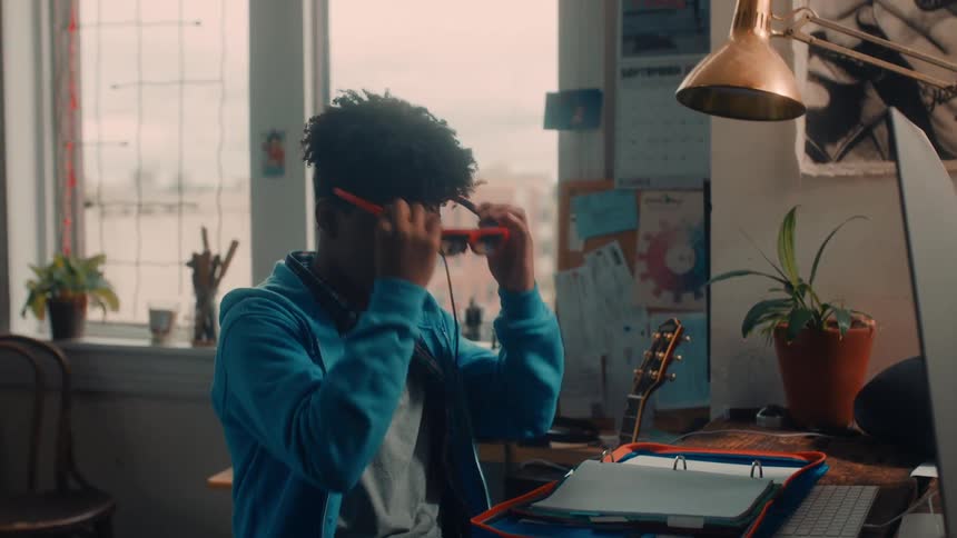 A teenager sitting at his desk doing homework puts on a virtual reality headset