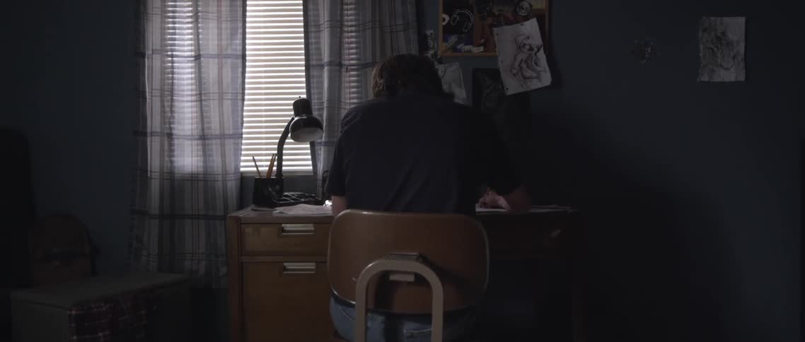 Male sitting in chair at a desk is writing on a piece of paper