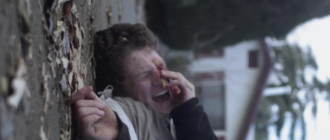 A young man with blood all over his face lies on the ground crying
