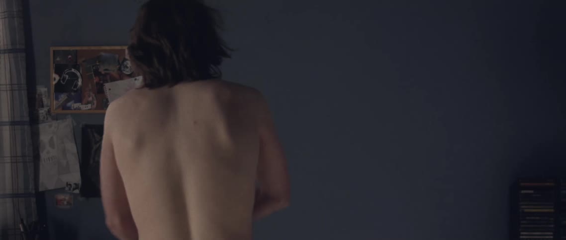 Caucasian male removing his shirt facing a wall