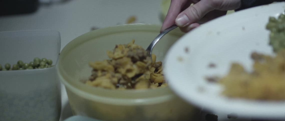 A person uses a spoon to scoop up food from a plastic container and places it on a plate