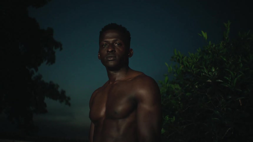 Topless African man near a green tree gazes ahead