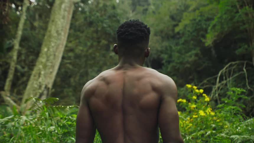 Muscular shirtless black man walking in a forest