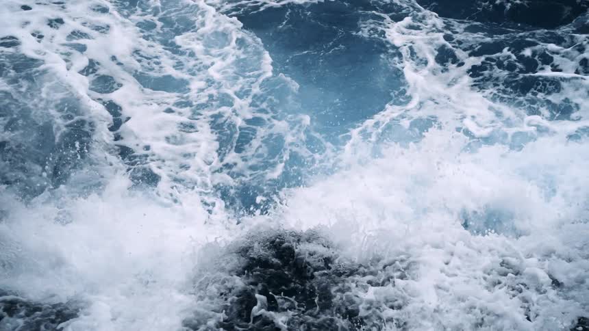 Drone view straight down of water crashing against rocks forming foam all over the surface