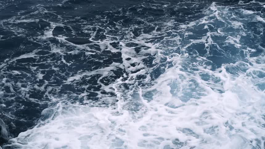 Aerial straight down of waves on the ocean crashing over themselves creating foam on the top