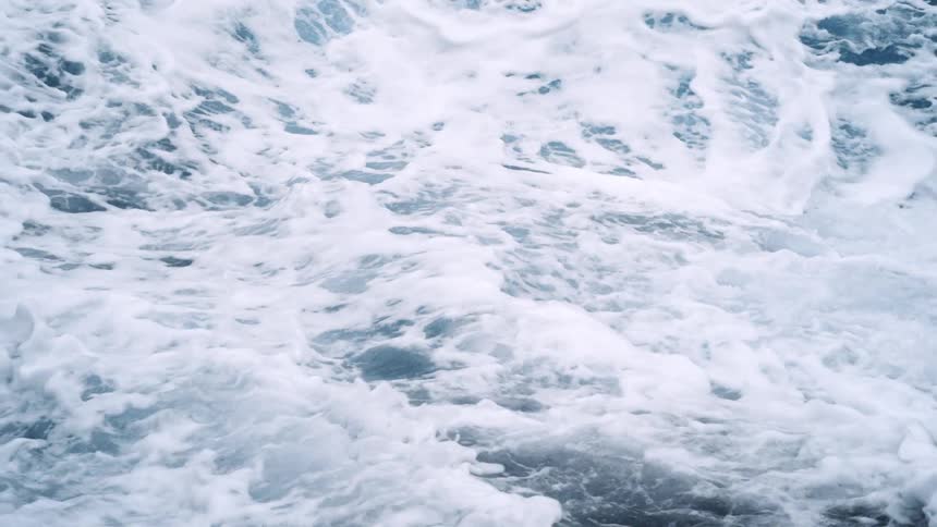 An aerial straight down of ocean waves crashing against rocks on the coast