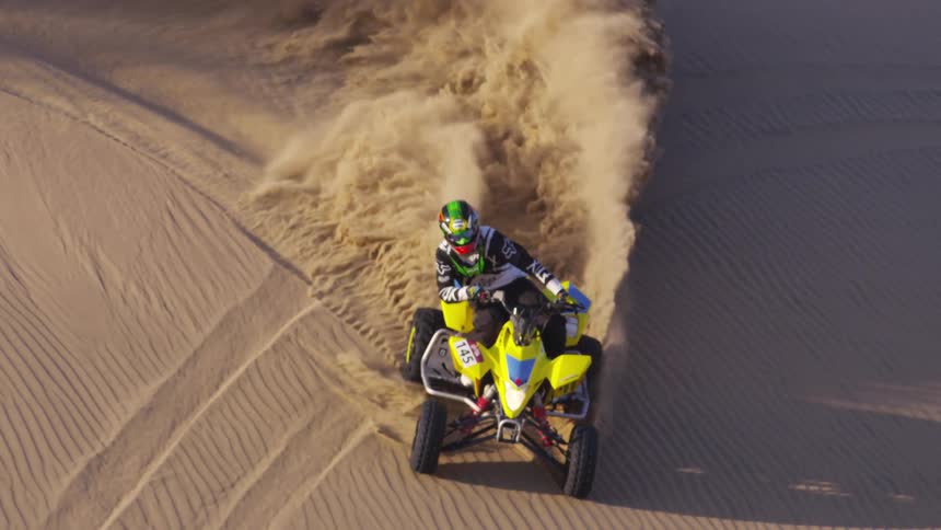 A person drifts a quad bike on a sand dune