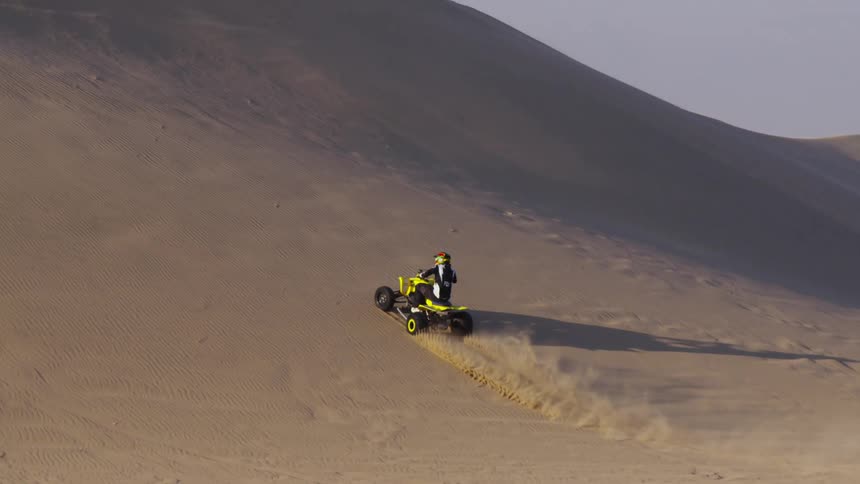 A four wheeler drives up a sand dune