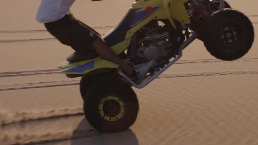 A man does a pop wheelie on a four wheeler