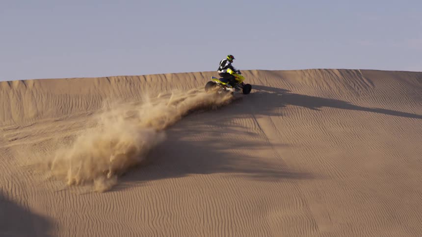 A person glides around a dune on a four wheeler