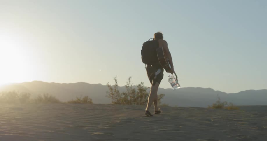 A man and woman walk across sand and brush