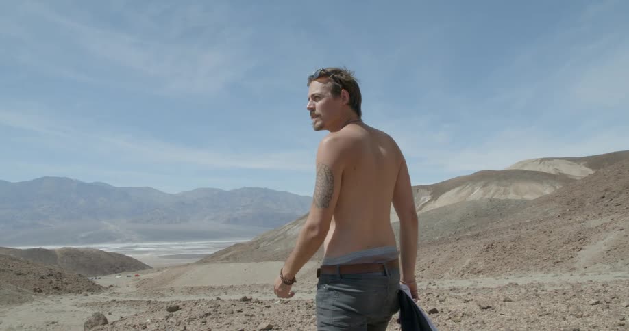 A man walks over a desert holding a camera