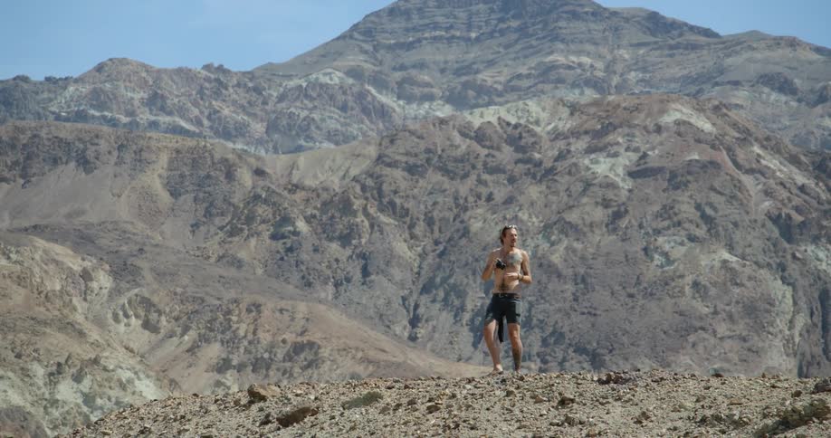 A man is standing on a mountain taking photographs of other mountains