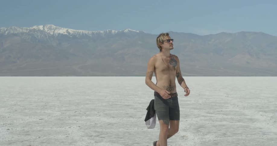 A man is walking over a white field shirtless