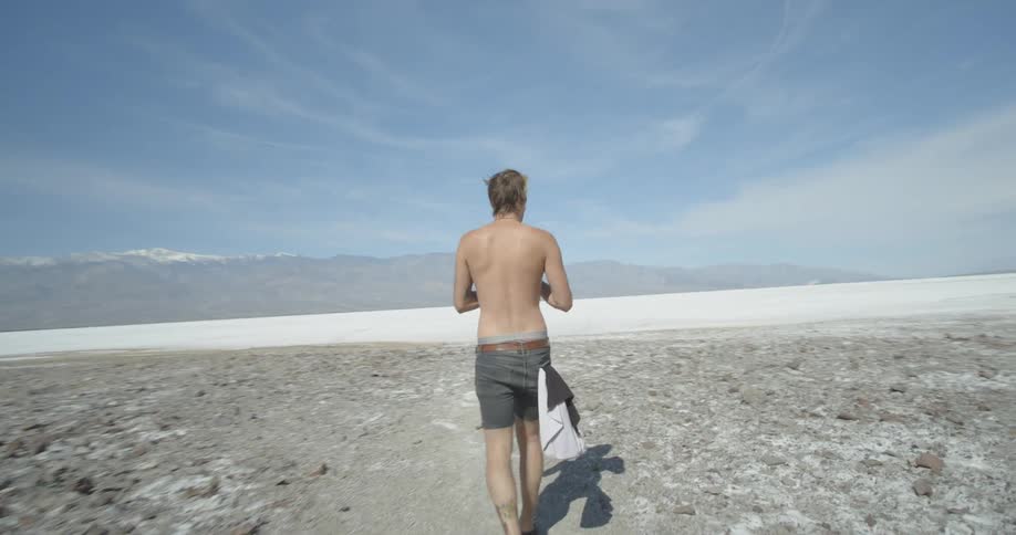 A man is walking over a barren field taking photographs