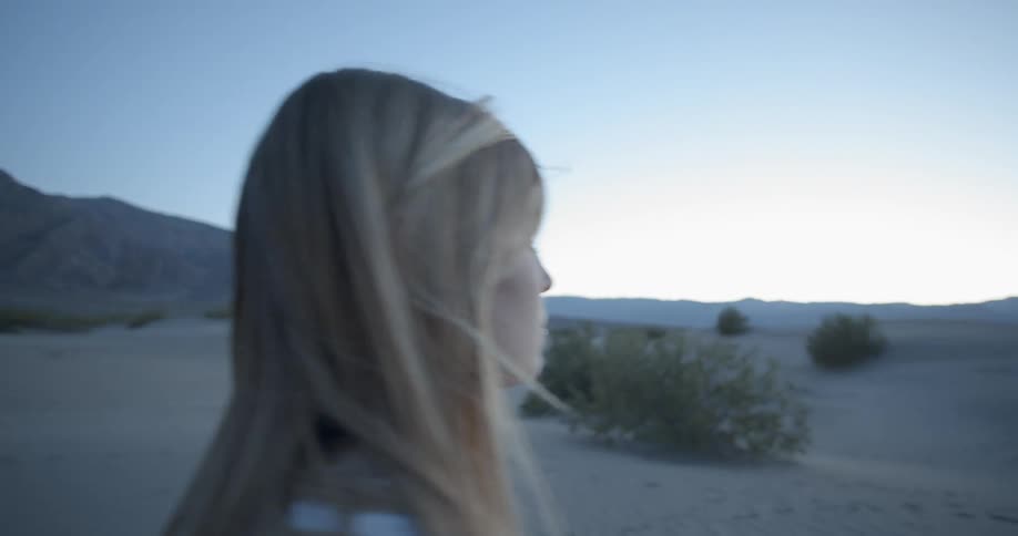 A woman brushes her hair back while walking in the desert