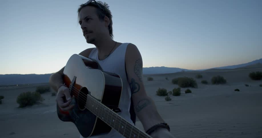 A man is playing a guitar in the desert at dawn