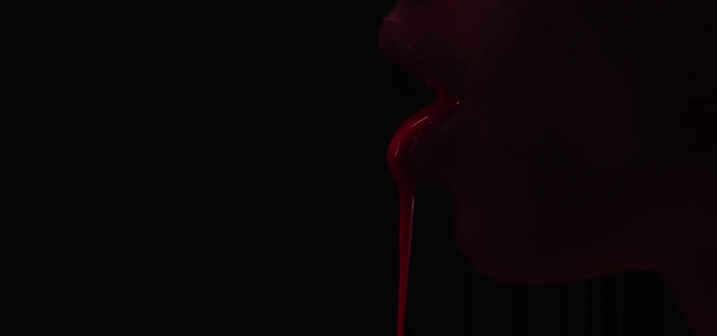 Red liquid pours out of a mouth in profile of a woman in front of a black background