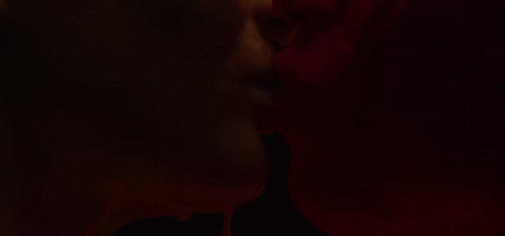Two people with melting wax on their faces kiss in the dark with a flickering light
