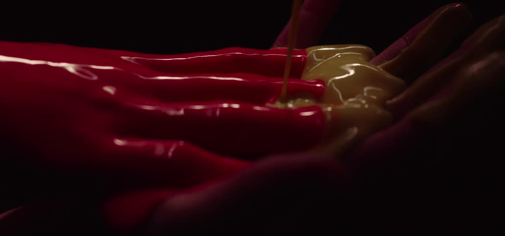 A person clasps their hands together as thick red and yellow paint drizzle over them