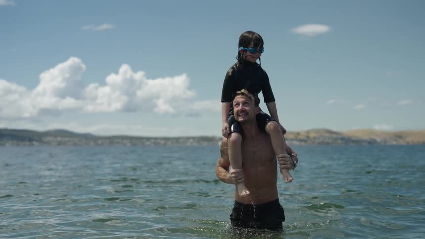 Dad carrying son on shoulders having fun in a lake