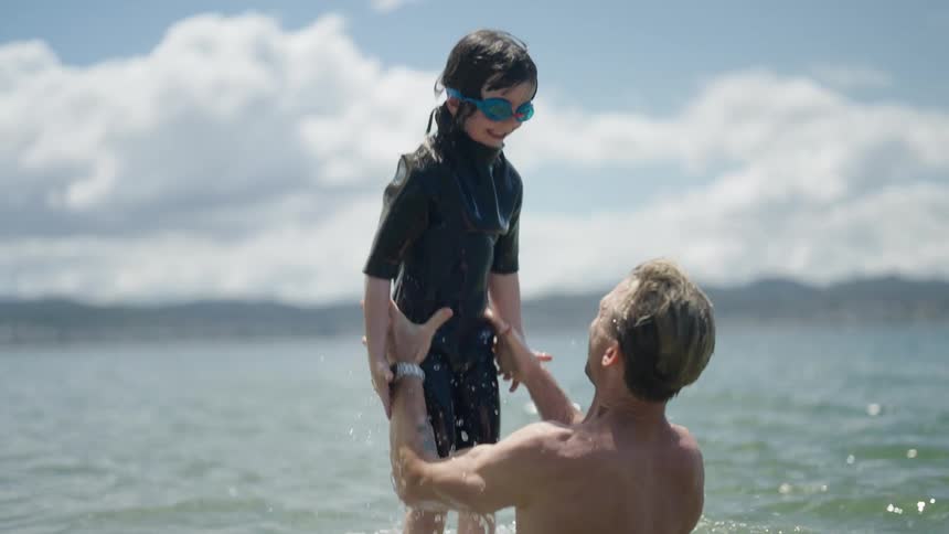 Man lifting his daugther from the water while both of them bathe at the sea