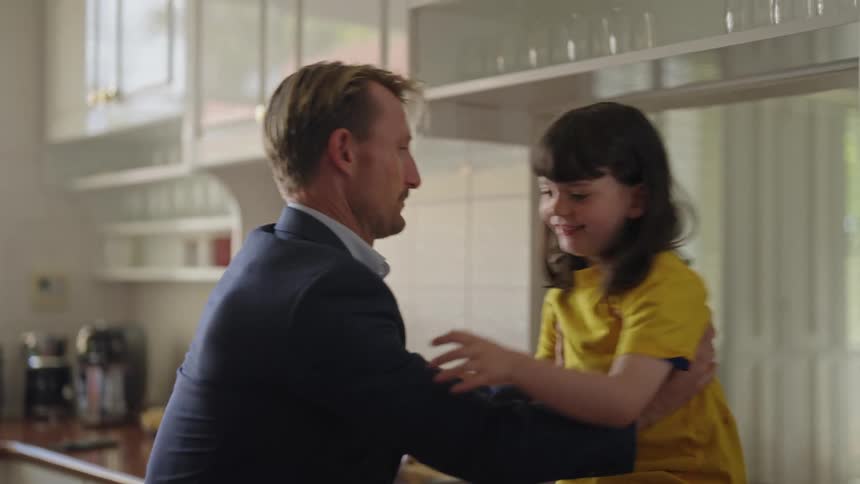 Father picks up daughter from kitchen counter and leaves room with her