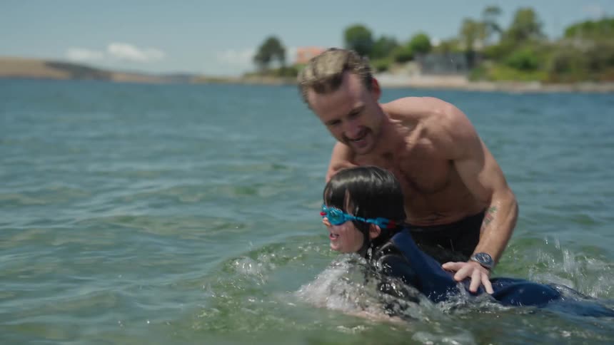 A father helps his daughter learn to swim in the calm waters of the bay both smiling when she is able to swim on her own