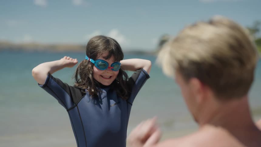 Father teaches daughter a hand routine as they stand on beach