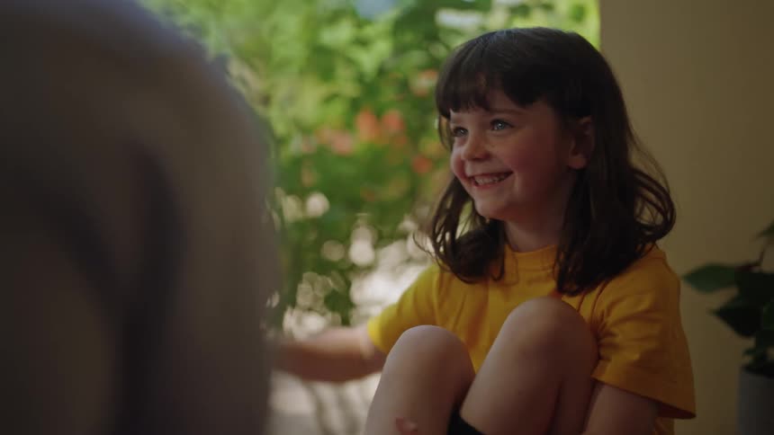 Girl sits on porch with adult smiling and gesturing