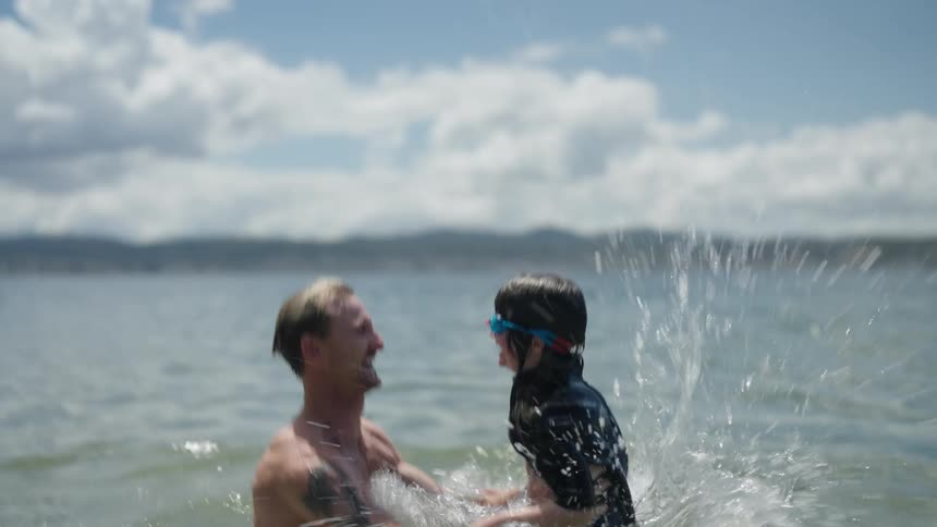 A man raises his daughter up and down from the water