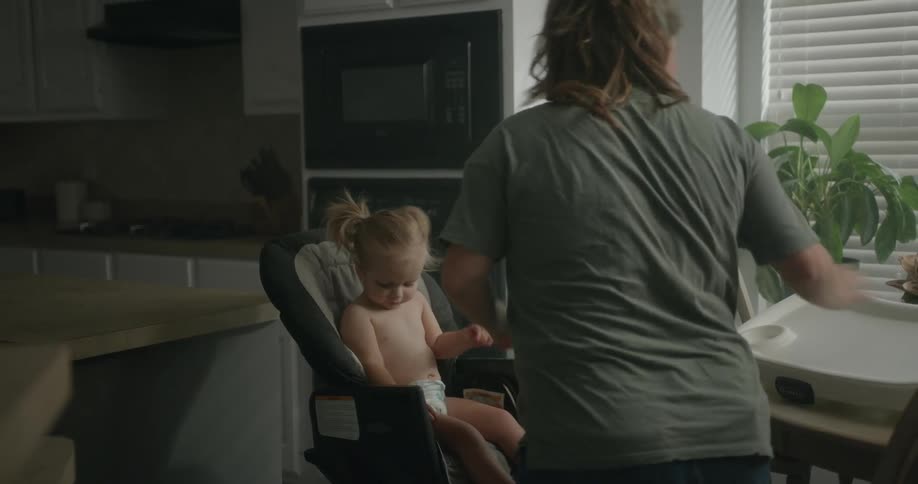 Pregnant mother secures daughter in high chair in breakfast nook near kitchen