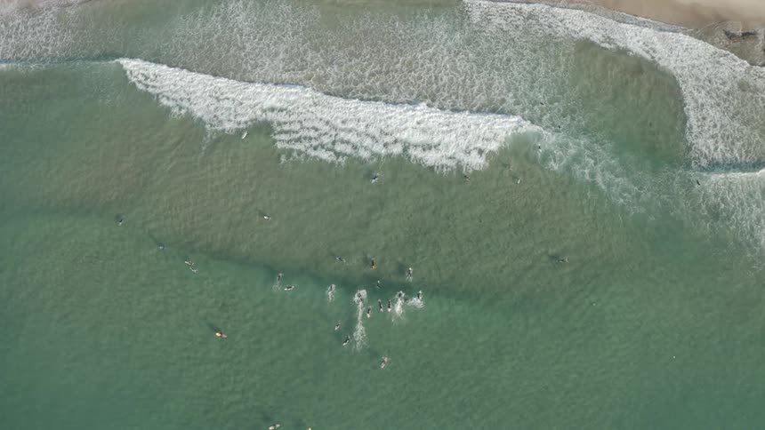 Ariel view of a beach with a lot of people in the water on surfboards