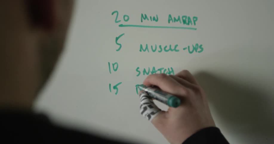 A man is writing his workout routine on a board